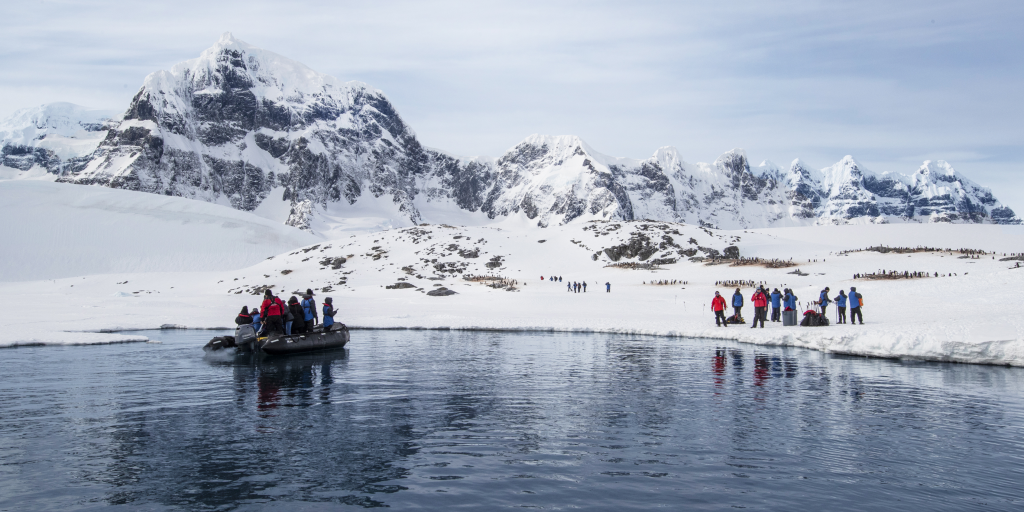 Expedition passengers in orange parkas stepping onto Antarctic shore from Zodiac boat