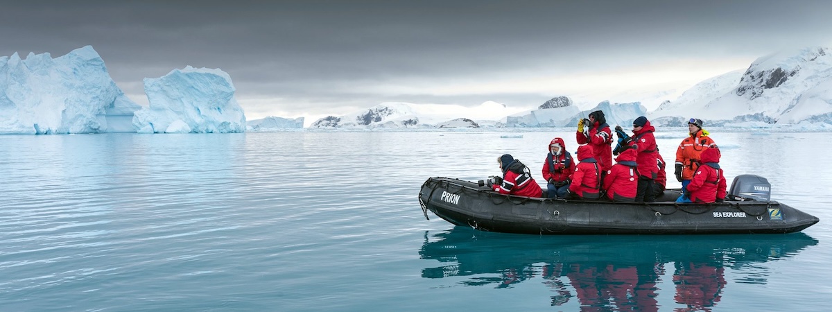 Zodiac boat navigating between Antarctic icebergs with expedition passengers